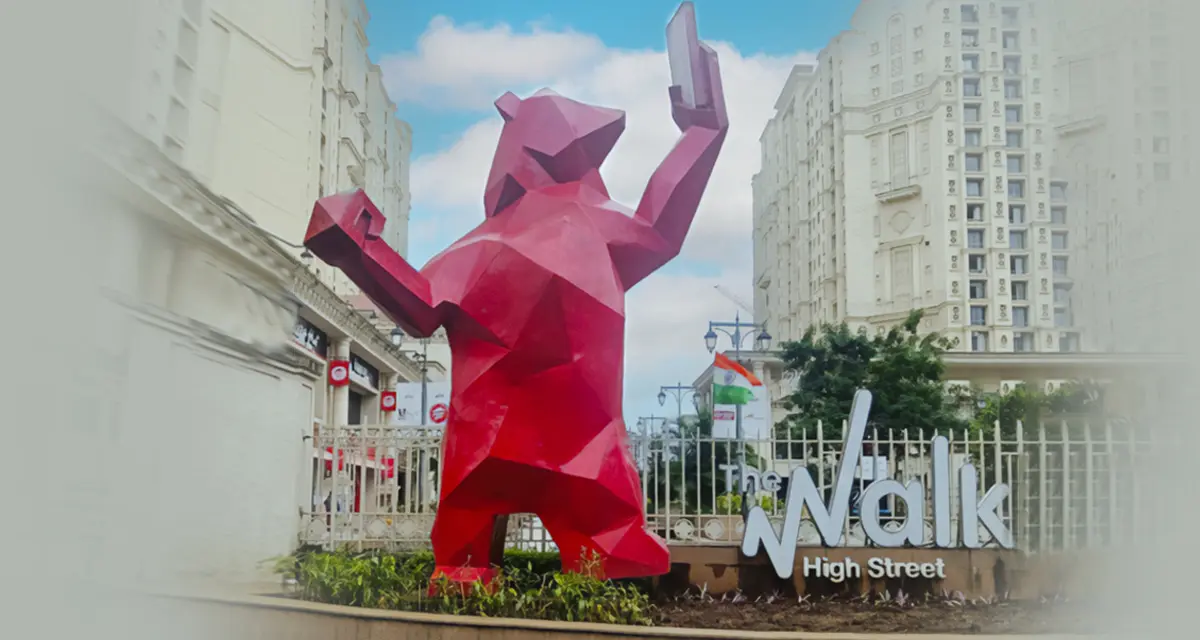 Vibrant red polygonal bear statue holding a phone, marking the entrance to 'The Walk High Street' urban area.